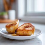 Two halves of caramelized baked pears drizzled with syrup, served on a small white plate.