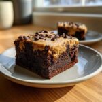 Close-up of a rich, dark chocolate banana bread brownies square topped with peanut butter frosting and chocolate chips.