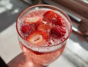 Close-up of a glass filled with sparkling pink champagne punch garnished with fresh strawberry slices and raspberries.