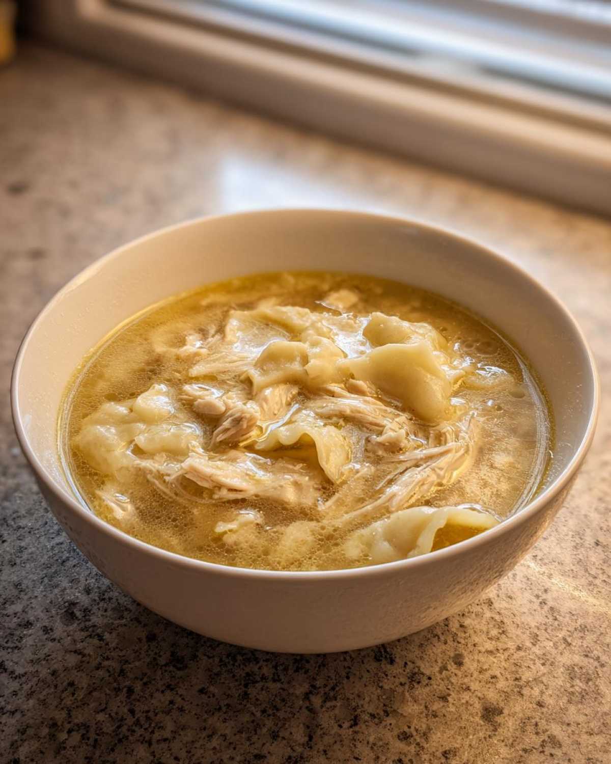 A close-up view of a white bowl filled with steaming chicken and dumplings in a rich broth.