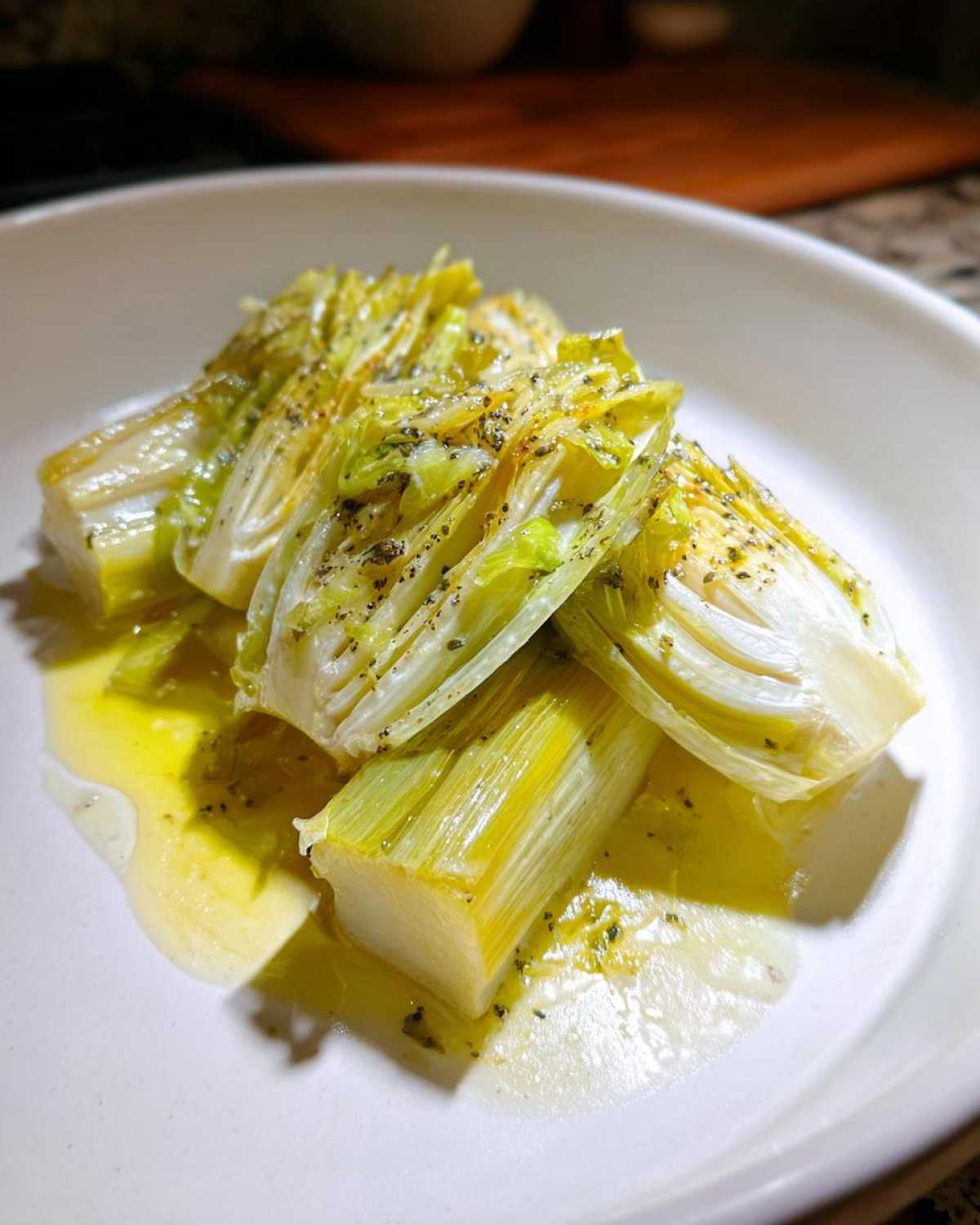 Close-up of tender braised leeks, cut into sections, served in a white bowl with melted butter and herbs.