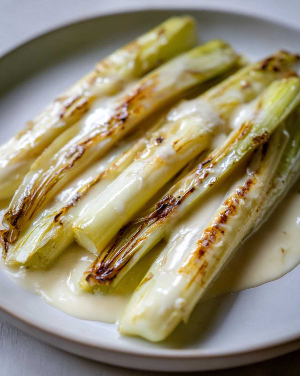 Close-up of tender braised leeks topped with a creamy white sauce, showing slight charring.