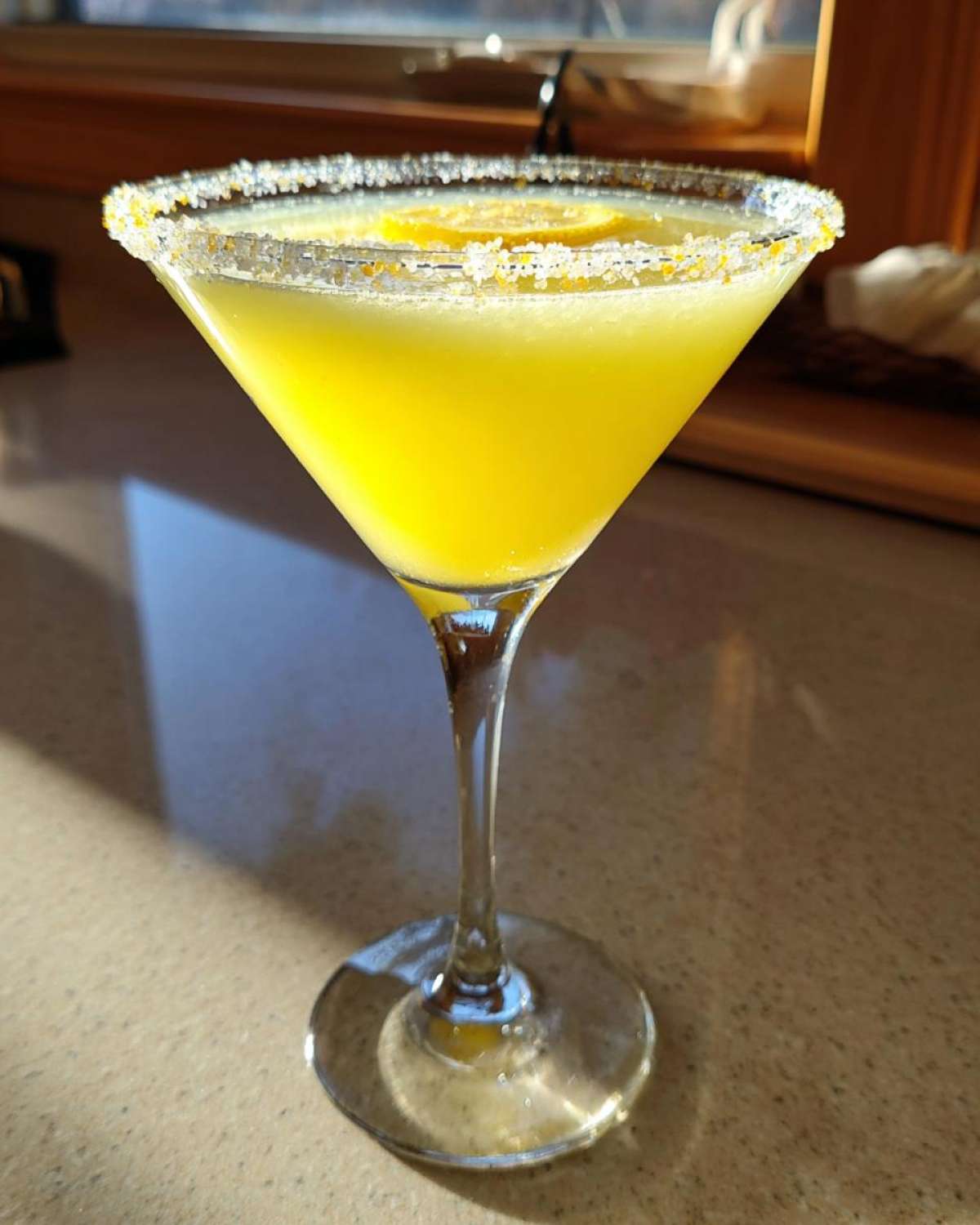A bright yellow lemon drop martini in a stemmed glass with a sugar-rim and lemon slice garnish.