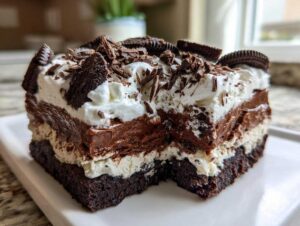A rich, layered slice of brownie refrigerator cake topped with whipped cream, chocolate shavings, and cookie pieces.