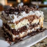 A decadent slice of brownie refrigerator cake showing multiple layers of dark chocolate cake, cream, and chocolate mousse, topped with whipped cream and shavings.