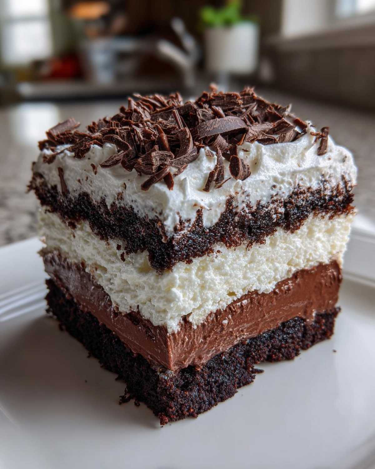 A decadent slice of brownie refrigerator cake showing layers of dark cake, chocolate pudding, whipped cream, and topped with chocolate shavings.