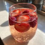 Close-up of a glass filled with sparkling pink champagne punch garnished with fresh sliced strawberries and whole raspberries.