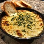 Close-up of hot, cheesy garlic bread dip in a small cast iron skillet, topped with parsley, with bread slices for dipping.