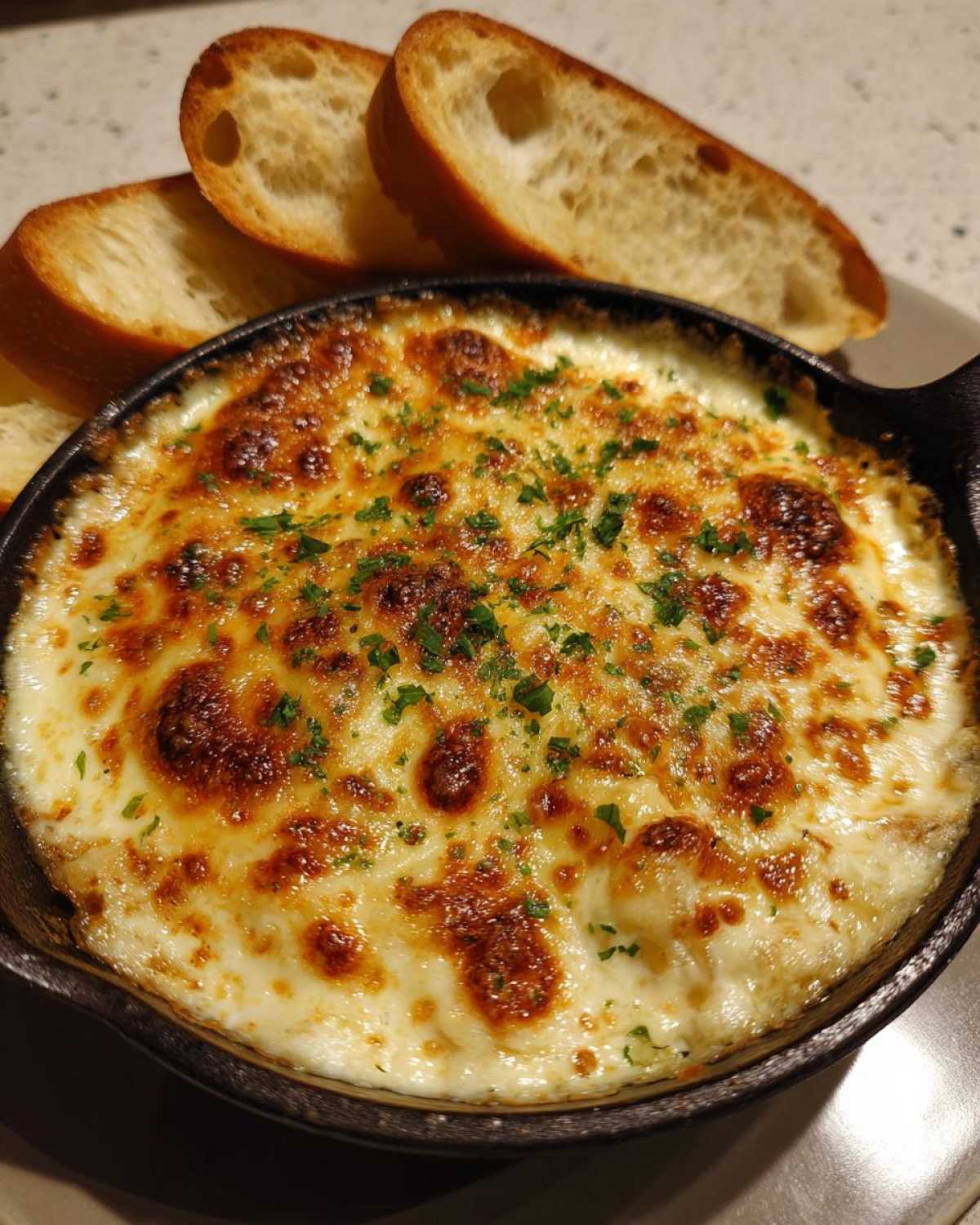 Close-up of a hot, bubbly cheesy garlic bread dip served in a small cast iron skillet with toasted bread slices.