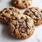 Close-up of four freshly baked, thick chocolate chip pudding cookies resting on a white marble surface.