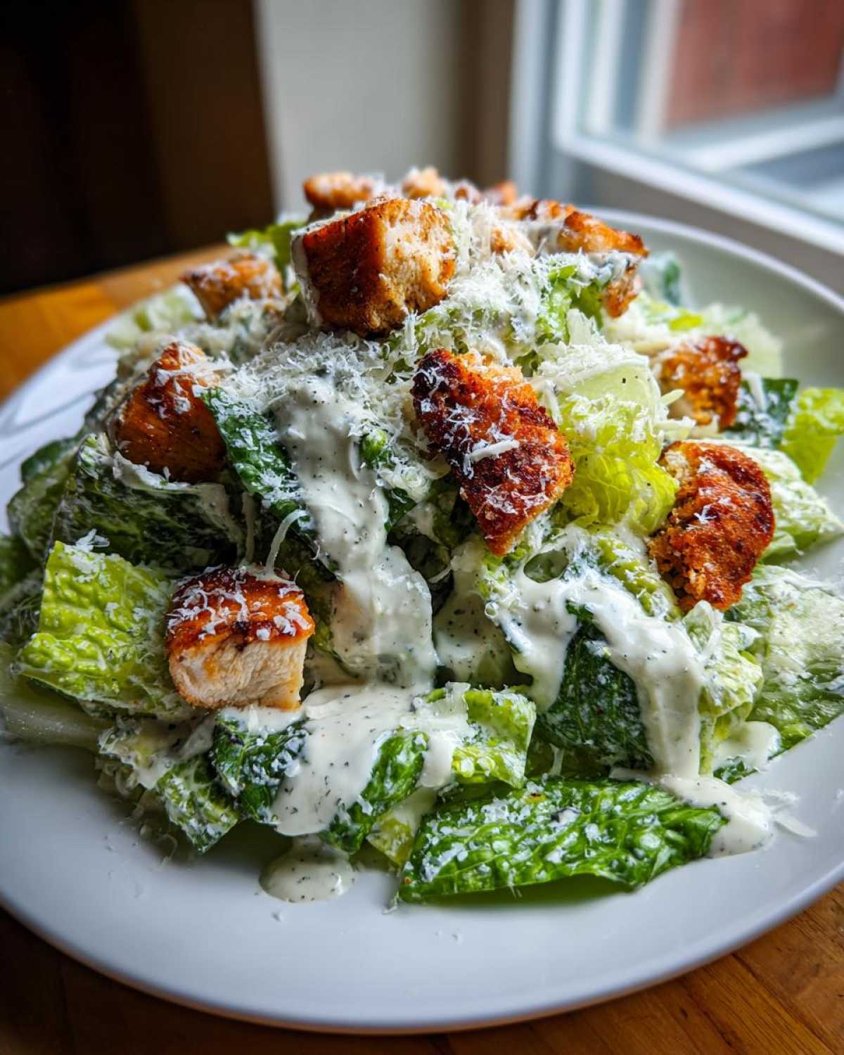 A close-up shot of a delicious chicken caesar salad topped with creamy dressing, grated parmesan, and golden croutons.