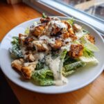 A close-up of a hearty chicken caesar salad topped with creamy dressing and grated parmesan cheese.