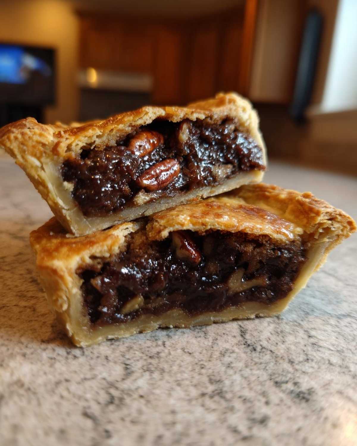 Two halves of a mini chocolate bourbon pecan pie showing the gooey dark filling and whole pecans inside the flaky crust.