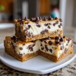 Three stacked slices of rich chocolate chip cheesecake bars with a graham cracker crust, topped with mini chocolate chips.