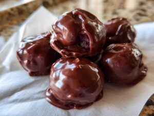 A small pile of glossy, dark chocolate covered cherries resting on white parchment paper.