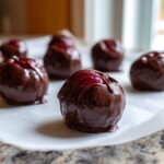 Close-up of several freshly made chocolate covered cherries cooling on white parchment paper.