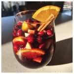 A glass filled with rich red Christmas sangria, loaded with cranberries, apple chunks, and orange slices, garnished with a cinnamon stick.