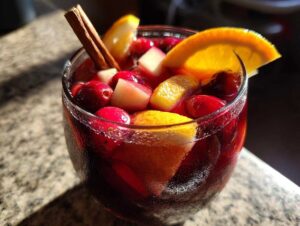Close-up of a glass filled with vibrant red Christmas sangria, garnished with cranberries, orange slices, and a cinnamon stick.