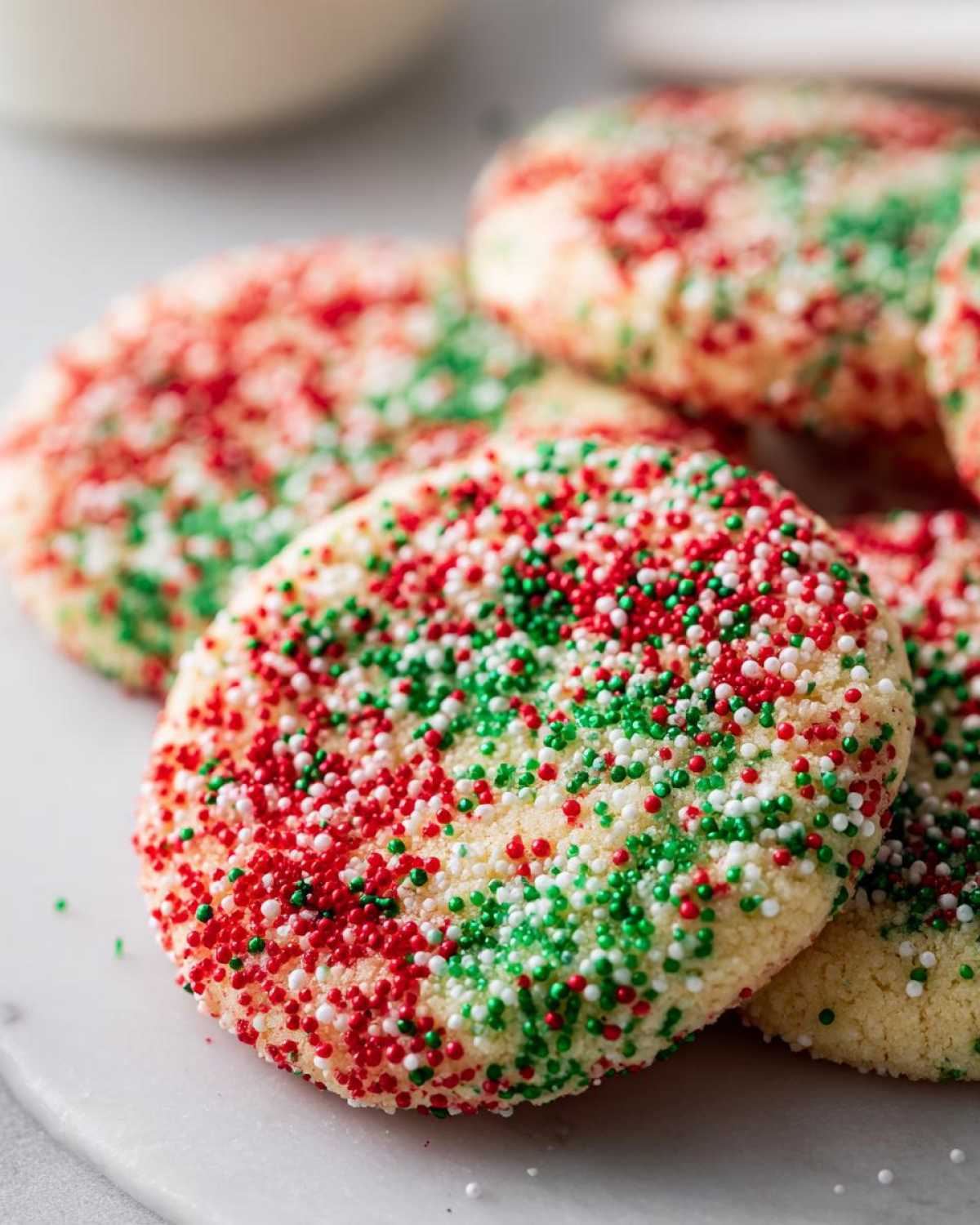 A close-up of freshly baked christmas sprinkle sugar cookies generously topped with red, green, and white nonpareils.