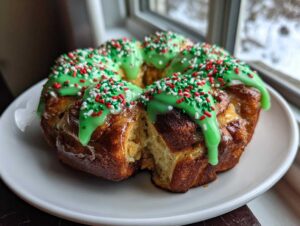 A ring of baked Christmas tree cinnamon rolls topped with bright green icing and red, white, and green sprinkles.