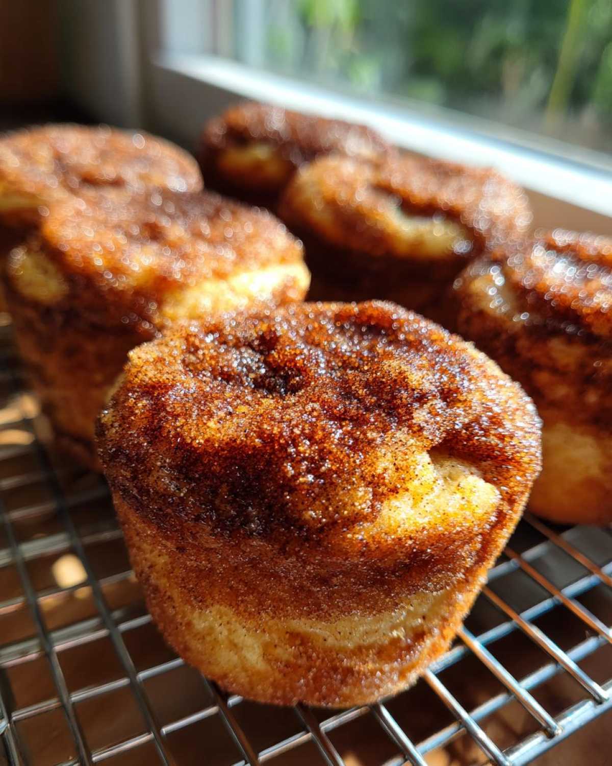 Close-up of several golden cinnamon sugar french toast muffins cooling on a wire rack near a window.