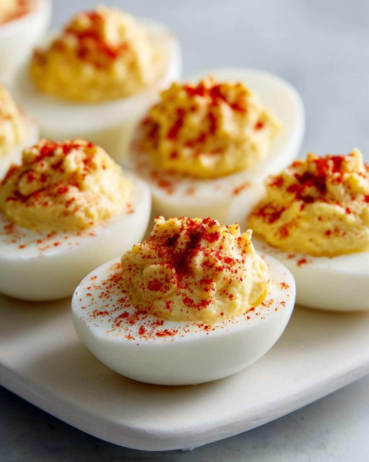 Close-up of several classic deviled eggs, filled with creamy yolk mixture and dusted generously with bright red paprika.