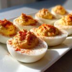 Close-up of several classic deviled eggs garnished with paprika, arranged on a white platter.