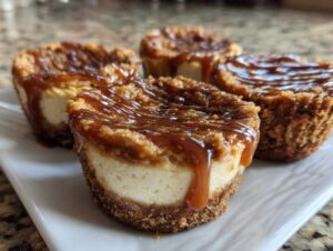 Four individual cookie butter cheesecake cups topped with a rich caramel drizzle, served on a white plate.