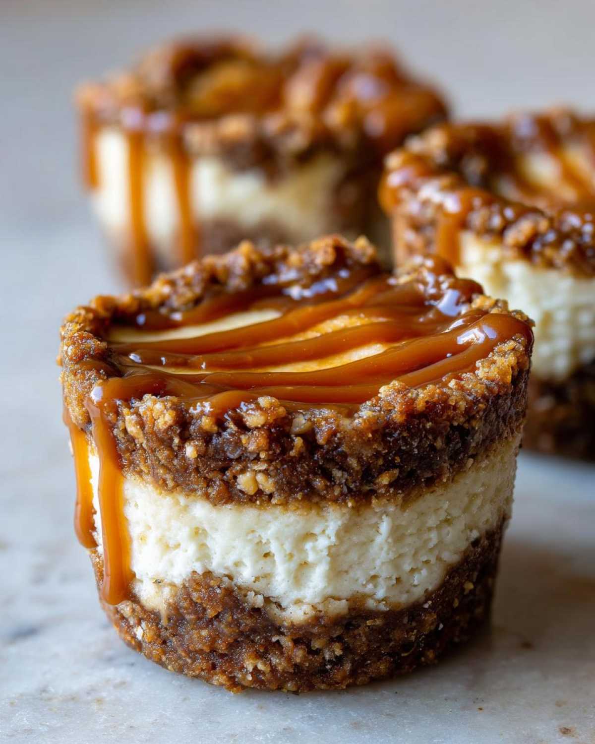 A close-up of a single cookie butter cheesecake cup showing layers of crust, creamy filling, and caramel drizzle.