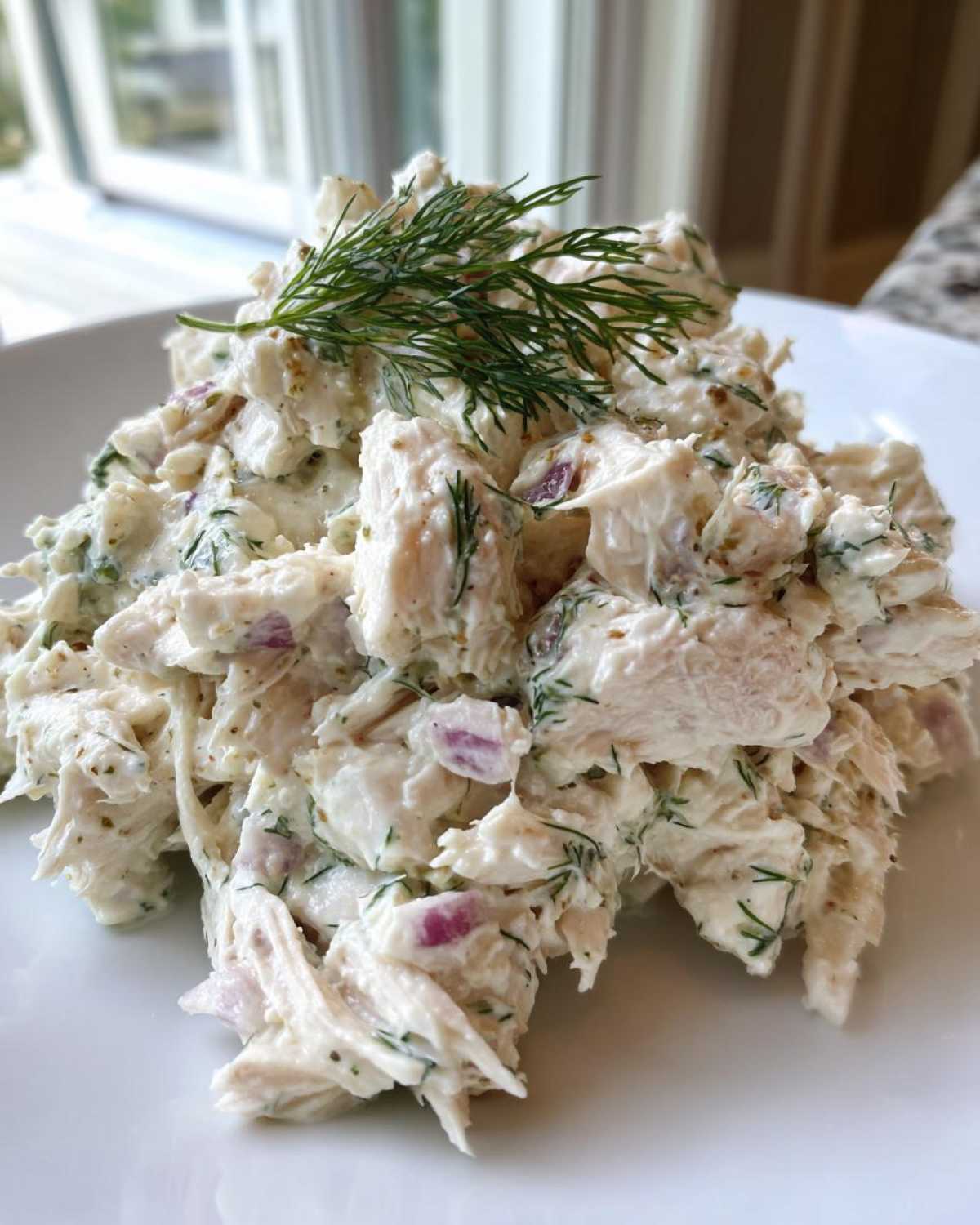 A close-up of a scoop of creamy cottage cheese chicken salad mixed with red onion and topped with fresh dill.