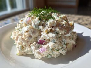 A mound of creamy cottage cheese chicken salad mixed with red onion and dill, served on a white plate.