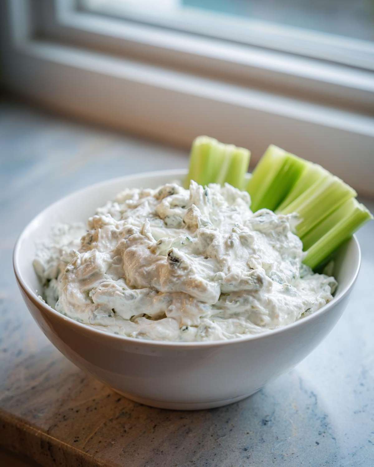 A white bowl filled with creamy blue cheese dip, garnished with celery sticks.