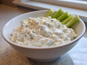 A white bowl filled with creamy blue cheese dip, served with fresh celery sticks for dipping.