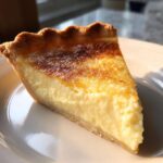 A close-up shot of a perfect slice of buttermilk pie on a white plate, showing the creamy filling and browned top.
