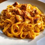 A close-up shot of creamy cajun chicken pasta featuring fettuccine noodles coated in a rich, orange sauce with chunks of seasoned chicken.