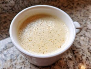 Close-up of creamy, frothy cauliflower soup served in a white mug on a granite countertop.