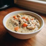 A close-up of a creamy chicken wild rice soup, featuring shredded chicken, diced carrots, and dark wild rice.