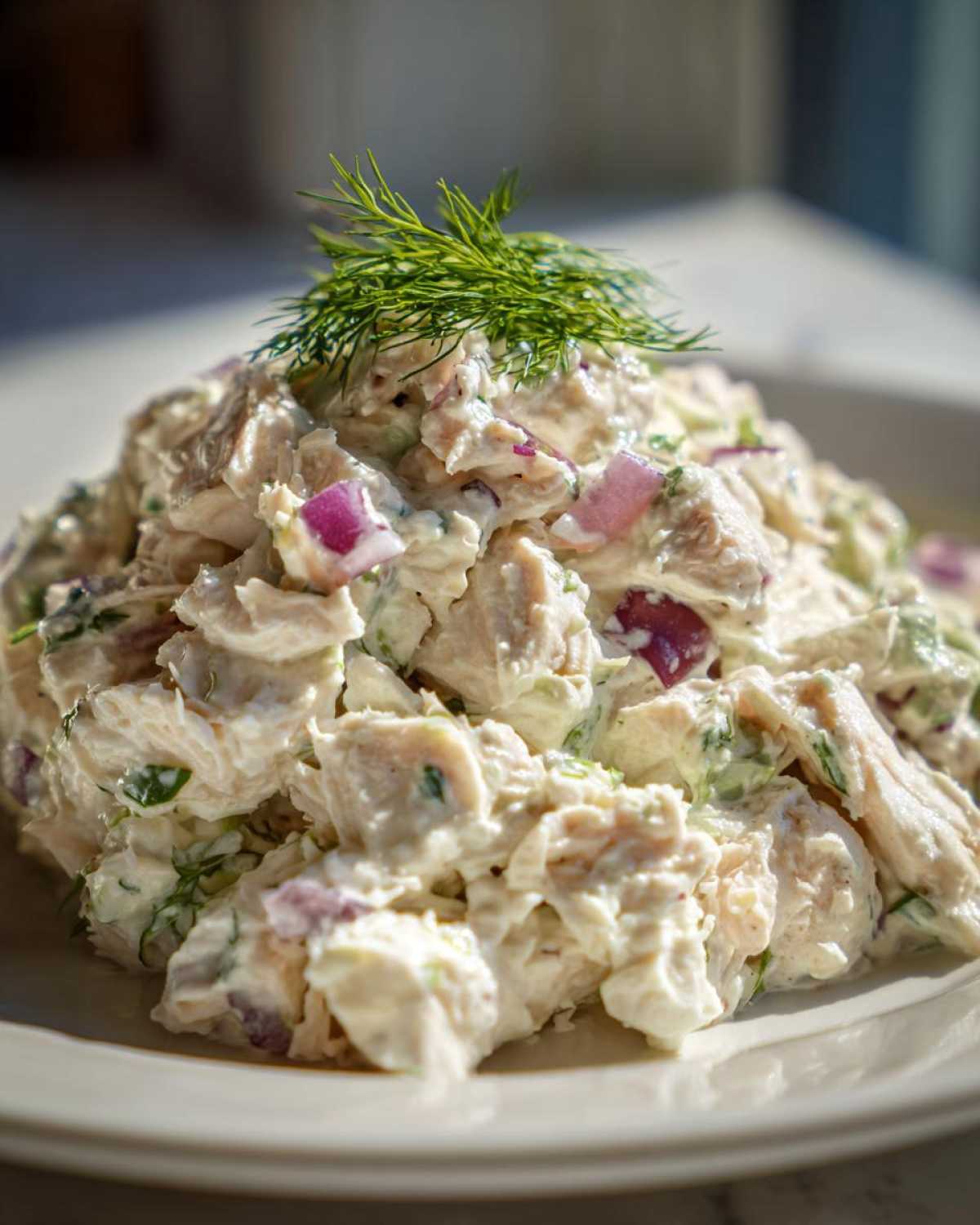 Close-up of creamy cottage cheese chicken salad mixed with red onion and topped with fresh dill.