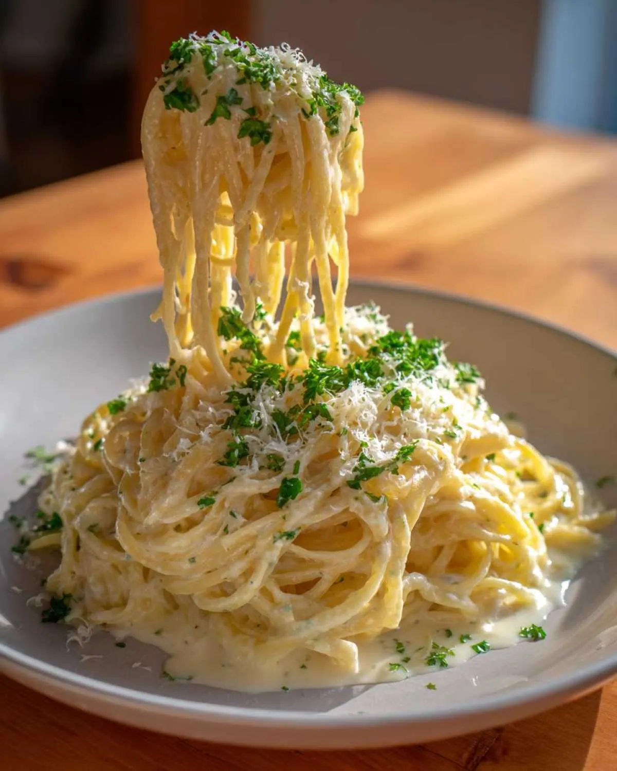 A fork lifting a large portion of creamy pasta coated in garlic parmesan sauce, topped with grated cheese and parsley.