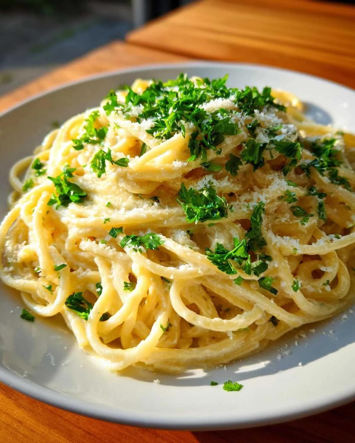 A close-up of creamy spaghetti coated in a rich sauce, topped with grated cheese and fresh parsley, representing garlic parmesan pasta.