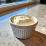 A small white ramekin filled with thick, creamy horseradish sauce speckled with herbs.