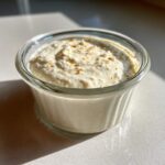 A small glass bowl filled with creamy horseradish sauce, garnished with a sprinkle of orange zest or spice.