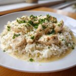A close-up of creamy one pot chicken and rice topped with fresh parsley on a white plate.