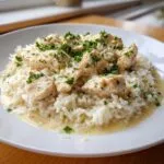 A close-up of creamy one pot chicken and rice topped with fresh parsley on a white plate.