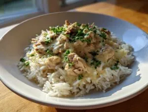 A close-up of creamy one pot chicken and rice served over white rice, garnished with fresh parsley.