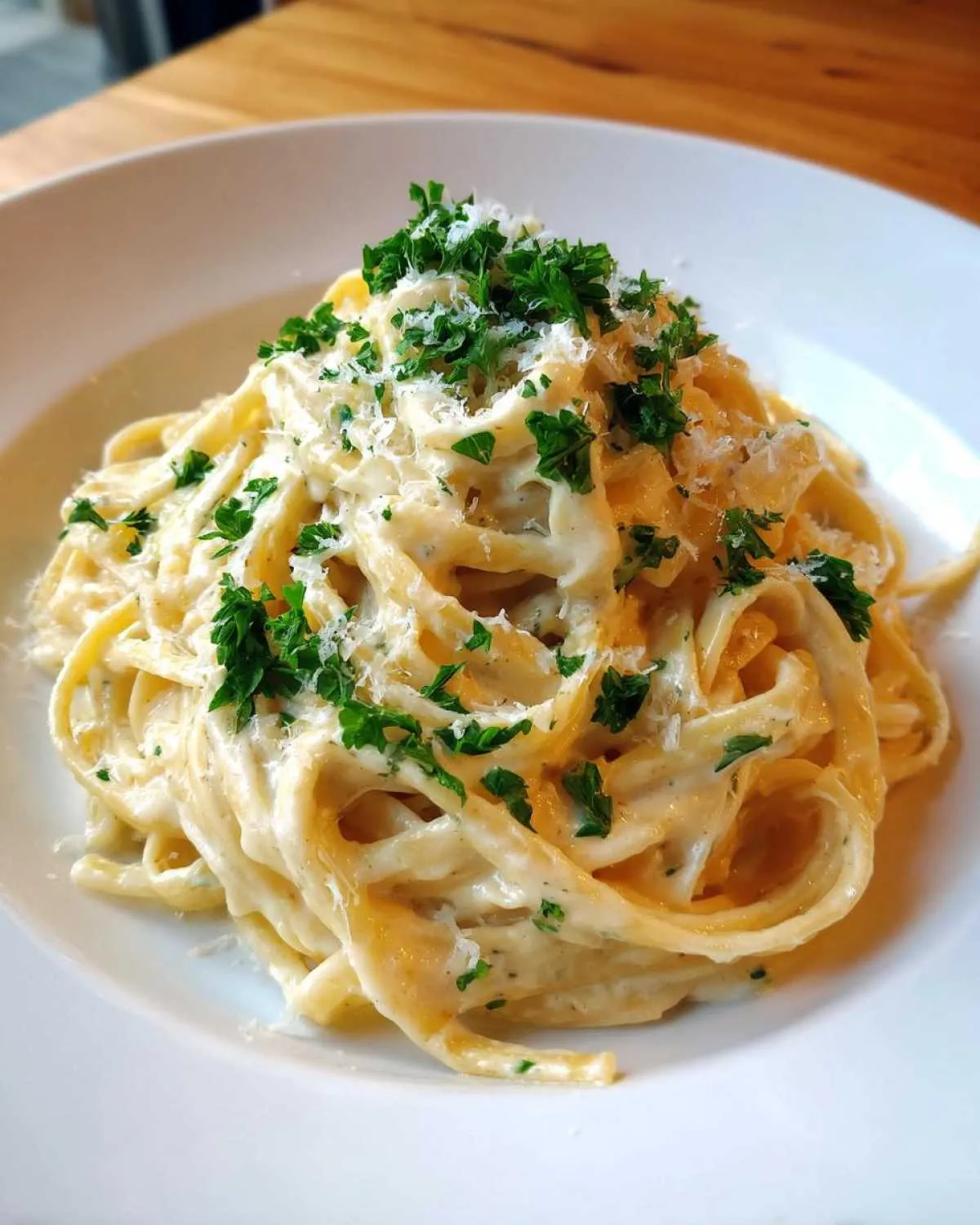 Close-up of fettuccine pasta coated in a creamy sauce, topped with grated cheese and fresh parsley, showcasing the garlic parmesan flavor.