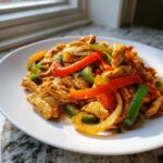 A close-up of seasoned shredded chicken mixed with vibrant strips of red and green bell peppers and onions, representing crockpot chicken fajitas.