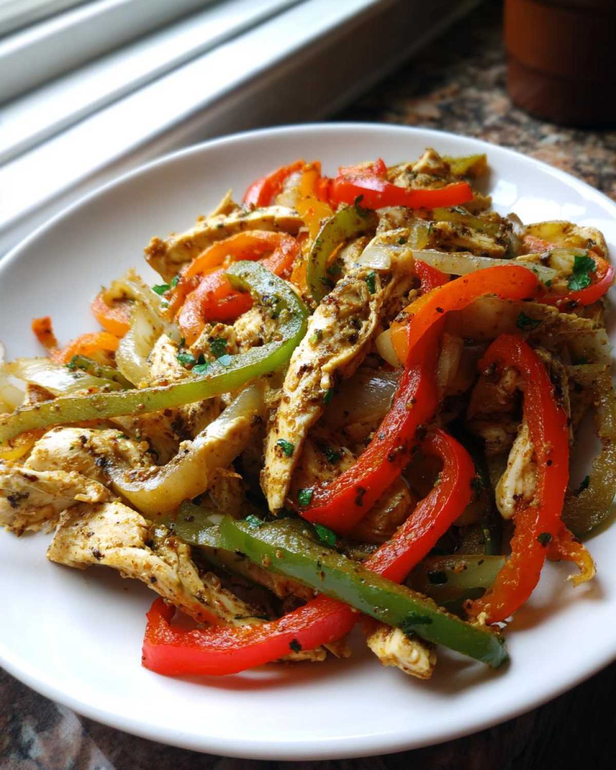 Close-up of seasoned chicken strips mixed with sautéed red, green, and yellow bell peppers and onions for crockpot chicken fajitas.
