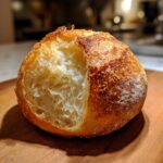 A rustic, golden-brown bread bowl with the top cut out, revealing a soft, airy interior, perfect for soup.