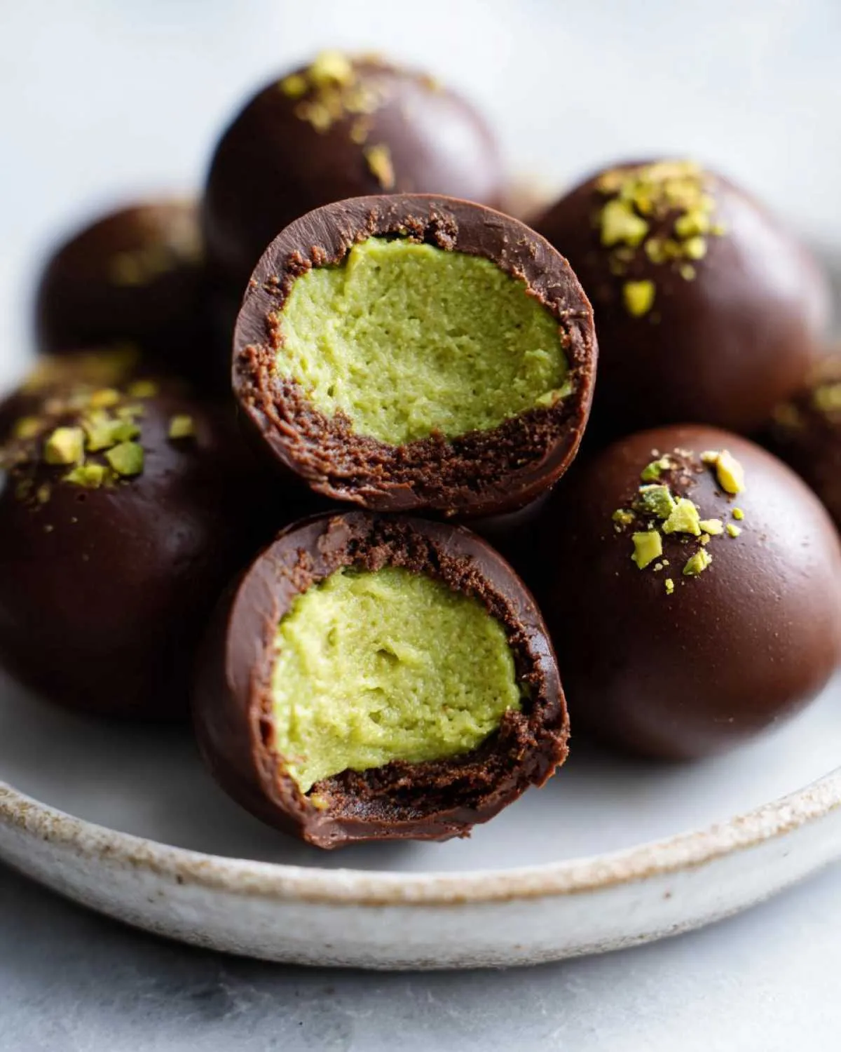 Close-up of dubai chocolate balls, one cut in half revealing a bright green pistachio filling inside a dark chocolate shell.